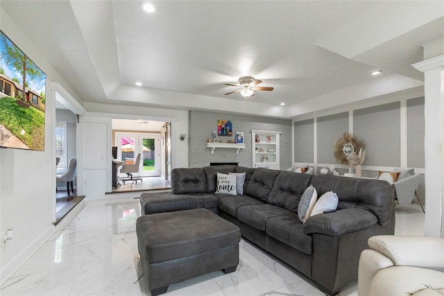 living area featuring ceiling fan, built in shelves, marble finish floor, a tray ceiling, and recessed lighting