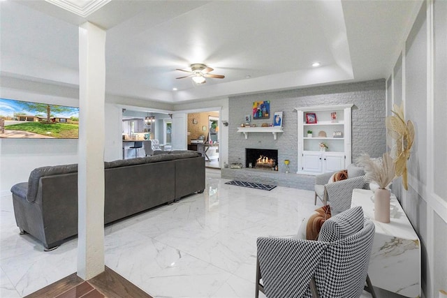 living room with a fireplace, built in features, a ceiling fan, recessed lighting, and a tray ceiling