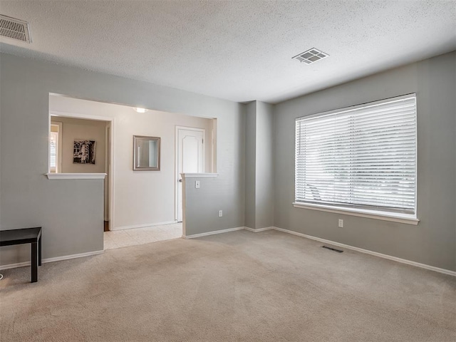 unfurnished room with a textured ceiling, visible vents, and light carpet