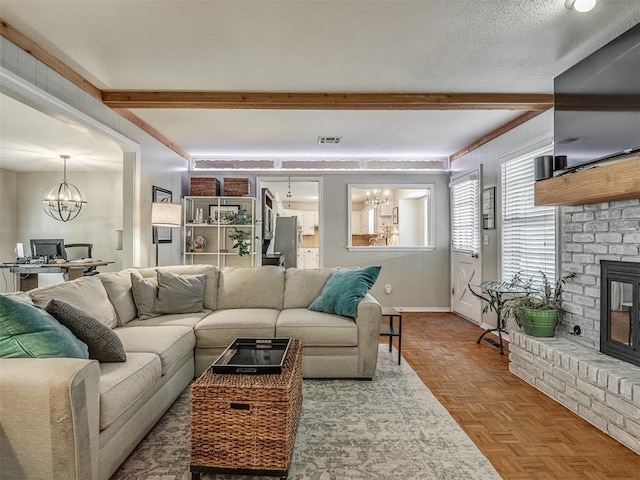 living room featuring a brick fireplace, a notable chandelier, beam ceiling, and visible vents