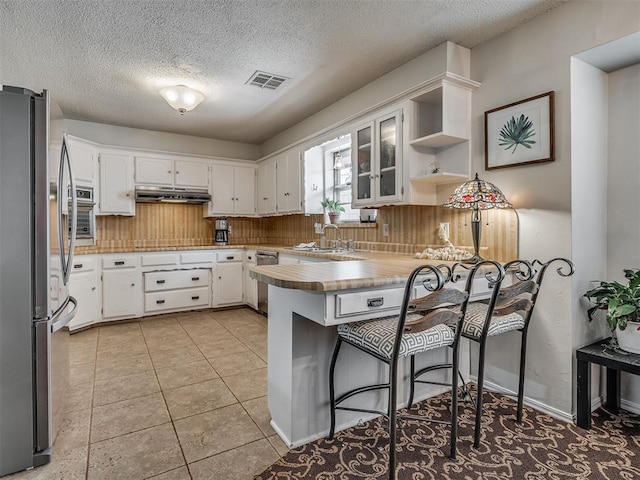 kitchen with visible vents, a peninsula, under cabinet range hood, a sink, and stainless steel appliances