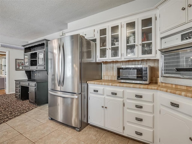 kitchen with decorative backsplash, a textured ceiling, appliances with stainless steel finishes, white cabinets, and glass insert cabinets