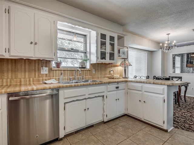 kitchen with dishwasher, a sink, a peninsula, a chandelier, and white cabinetry