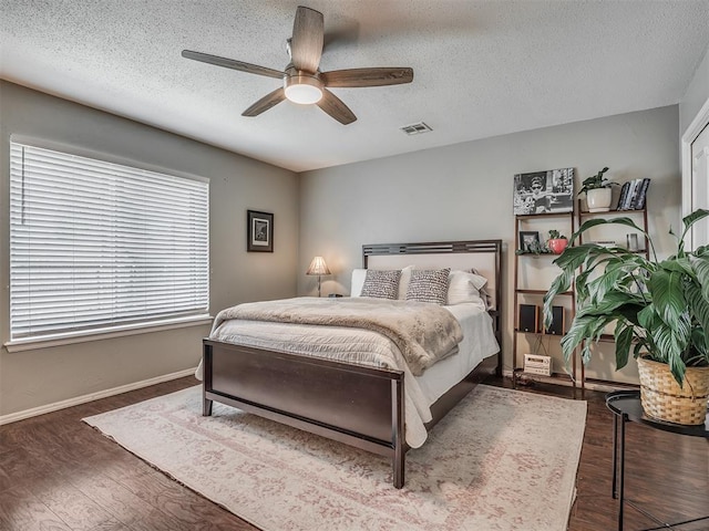 bedroom featuring a ceiling fan, a textured ceiling, visible vents, wood finished floors, and baseboards