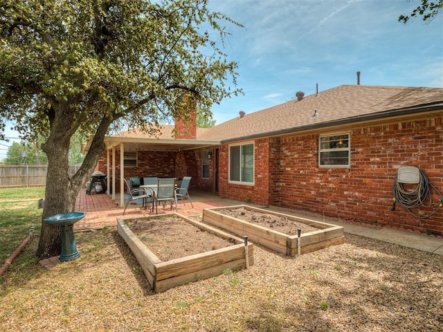 back of property featuring a chimney, a garden, roof with shingles, brick siding, and fence
