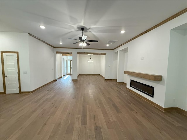 unfurnished living room featuring wood finished floors, ceiling fan, a glass covered fireplace, visible vents, and crown molding