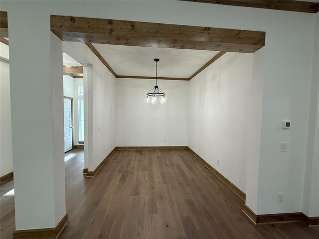 unfurnished dining area with beam ceiling, wood finished floors, ornamental molding, and baseboards