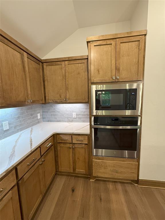 kitchen with built in microwave, brown cabinets, lofted ceiling, oven, and wood finished floors