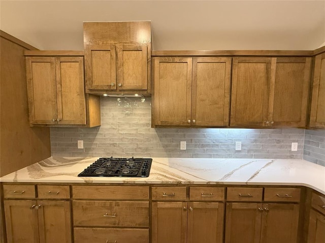 kitchen featuring black gas cooktop, brown cabinets, light stone countertops, and backsplash