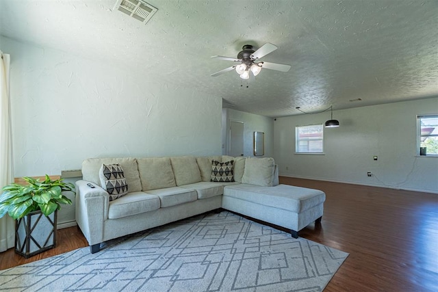 living room featuring wood finished floors, a textured ceiling, a ceiling fan, and visible vents
