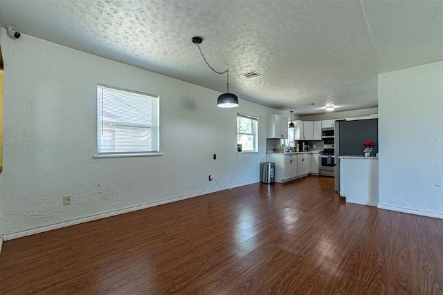unfurnished living room featuring a textured ceiling, a textured wall, dark wood finished floors, baseboards, and visible vents