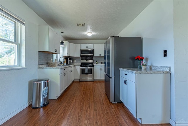 kitchen with stainless steel appliances, dark wood-style floors, a textured ceiling, a sink, and visible vents