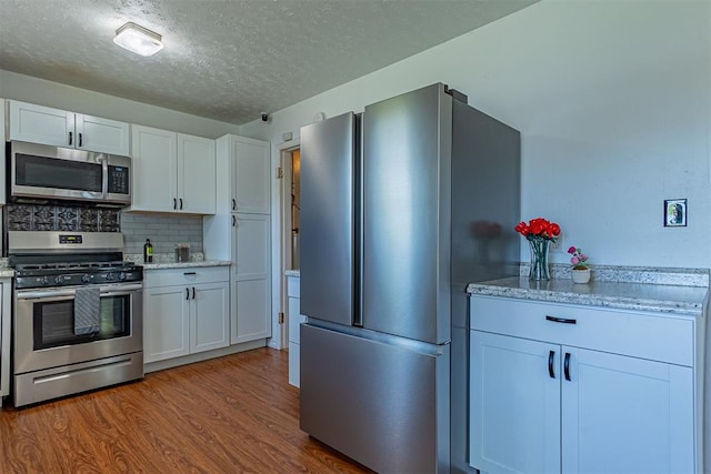 kitchen featuring a textured ceiling, tasteful backsplash, white cabinetry, wood finished floors, and appliances with stainless steel finishes