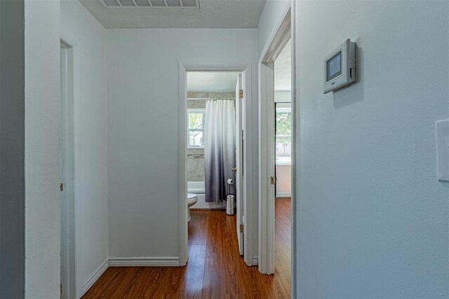 hall with wood finished floors, visible vents, and baseboards