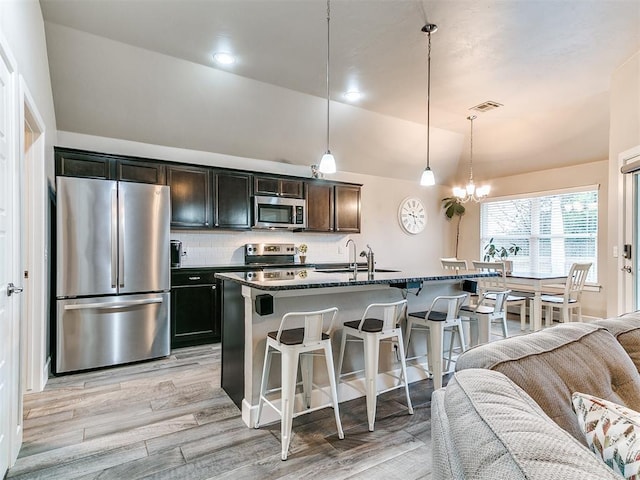 kitchen featuring vaulted ceiling, a sink, light wood finished floors, a breakfast bar, and stainless steel appliances