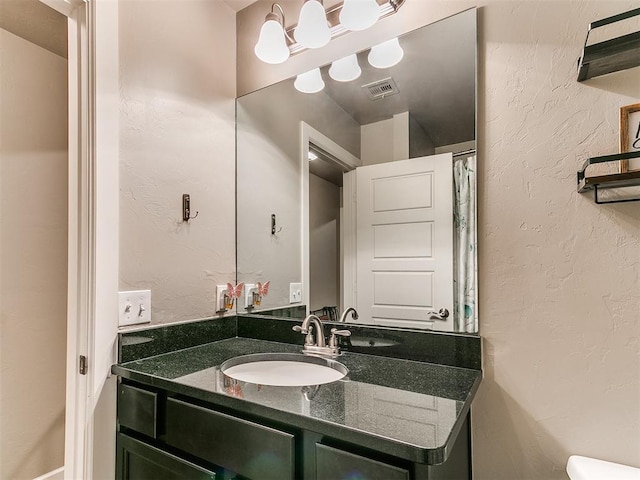 bathroom with toilet, a textured wall, visible vents, and vanity