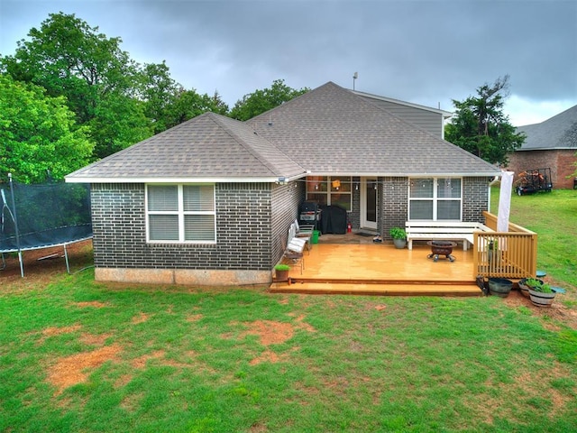 rear view of property featuring a lawn, a trampoline, roof with shingles, and a deck