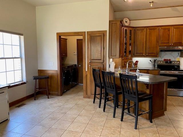 kitchen featuring stainless steel electric range, dark countertops, brown cabinets, a breakfast bar, and under cabinet range hood