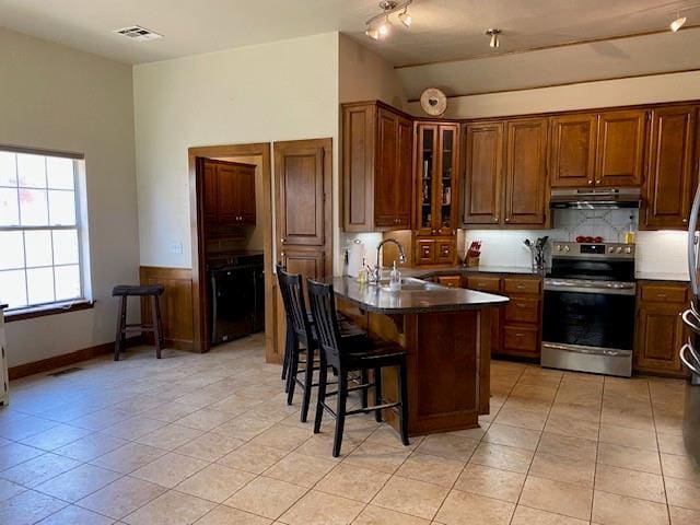 kitchen featuring a kitchen breakfast bar, under cabinet range hood, visible vents, decorative backsplash, and electric range