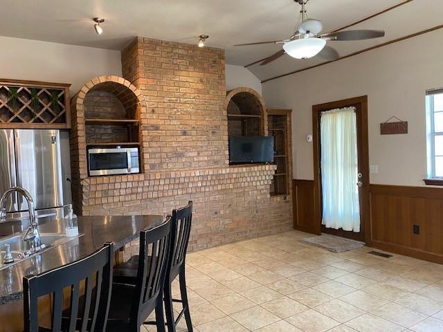 dining space with light tile patterned flooring, vaulted ceiling, a ceiling fan, and wainscoting