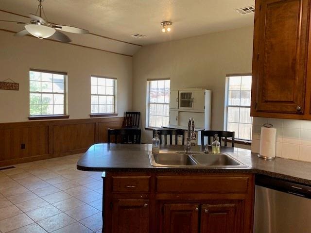 kitchen with vaulted ceiling, stainless steel dishwasher, dark countertops, a sink, and a peninsula
