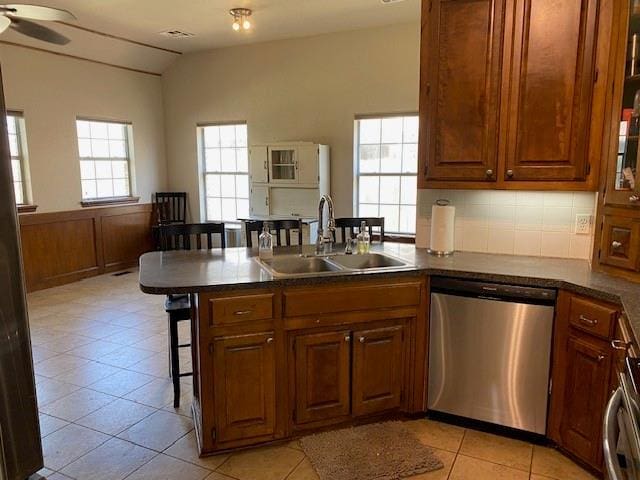 kitchen featuring a peninsula, stainless steel dishwasher, a sink, vaulted ceiling, and a breakfast bar area