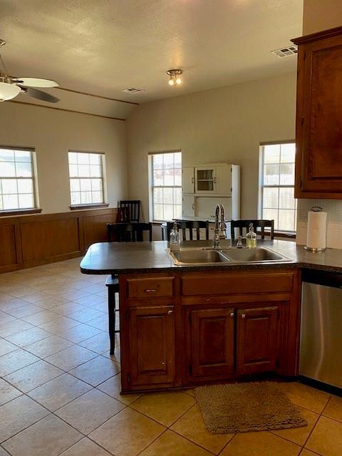 kitchen with a breakfast bar, dishwasher, visible vents, light tile patterned floors, and a sink