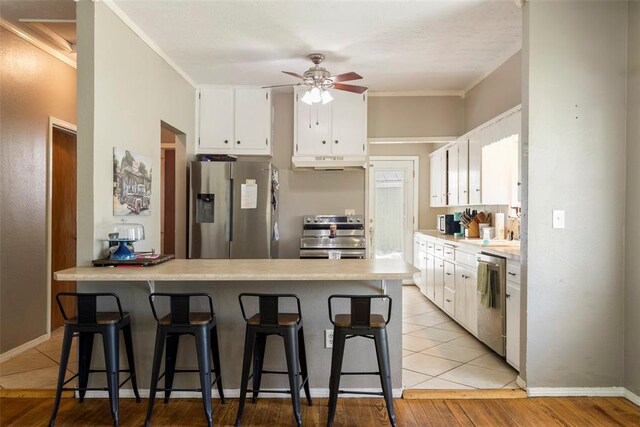 724 Maple St, Perry, OK 73077 - kitchen featuring under cabinet range hood, stainless steel appliances, white cabinetry, and a kitchen breakfast bar