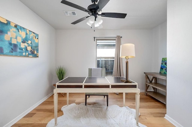 office area with baseboards, a ceiling fan, visible vents, and light wood finished floors