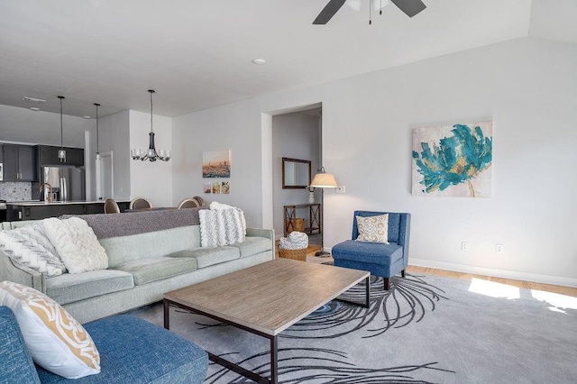 living room featuring ceiling fan with notable chandelier, baseboards, and light wood-style floors