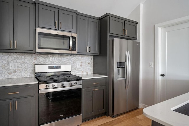 kitchen featuring tasteful backsplash, light wood-type flooring, gray cabinets, baseboards, and appliances with stainless steel finishes