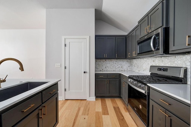 kitchen with stainless steel appliances, a sink, light wood-type flooring, vaulted ceiling, and light countertops