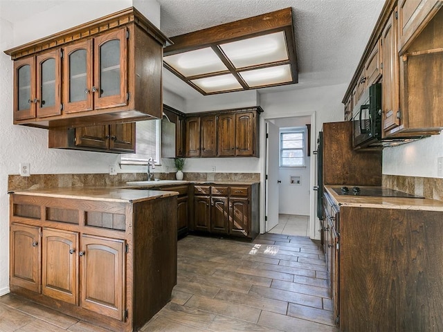 11609 Windmill Rd, Oklahoma City, OK 73162 - kitchen featuring a sink, a textured ceiling, black appliances, glass insert cabinets, and a peninsula