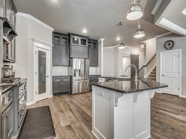 kitchen with stainless steel fridge, decorative backsplash, crown molding, a breakfast bar, and an island with sink