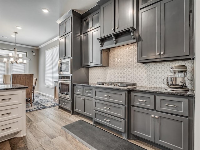 kitchen featuring dark stone counters, crown molding, decorative backsplash, stainless steel appliances, and a notable chandelier