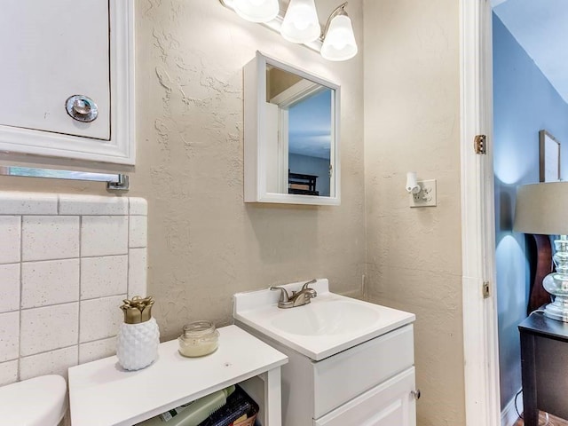 half bathroom with toilet, a textured wall, and vanity