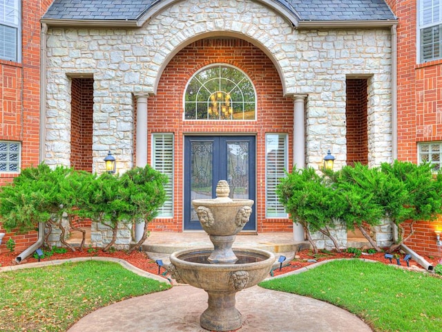 property entrance featuring brick siding, a high end roof, french doors, and stone siding