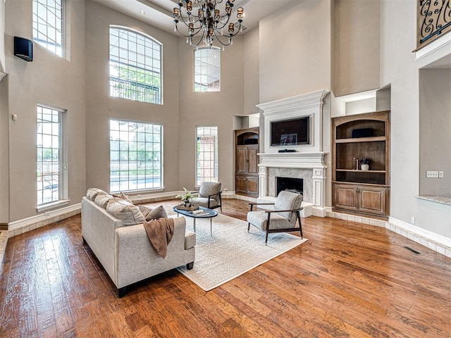 living room featuring baseboards, a chandelier, a high ceiling, hardwood / wood-style floors, and a premium fireplace