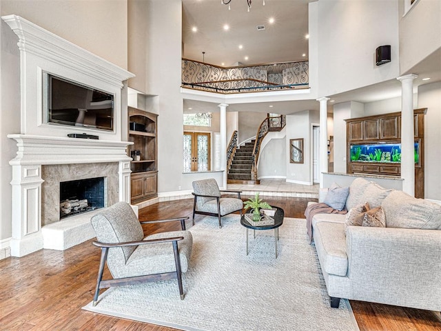 living room with decorative columns, wood finished floors, baseboards, a high ceiling, and recessed lighting