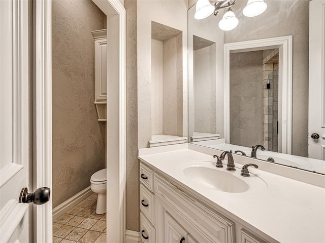 bathroom with vanity, a textured wall, baseboards, and toilet