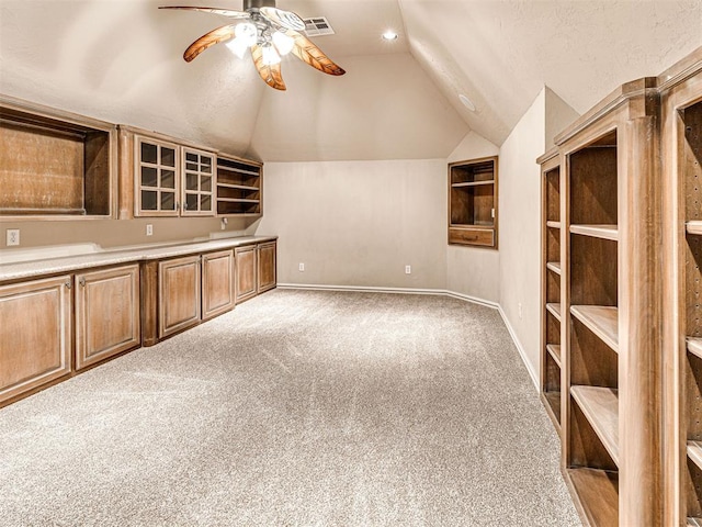 interior space featuring ceiling fan, built in features, baseboards, lofted ceiling, and carpet