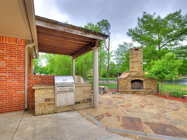 view of patio with fence, area for grilling, and an outdoor stone fireplace