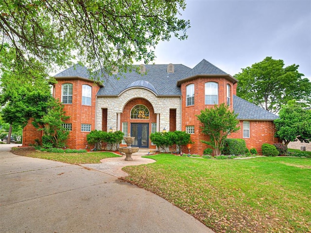 french country inspired facade with brick siding, a shingled roof, and a front yard