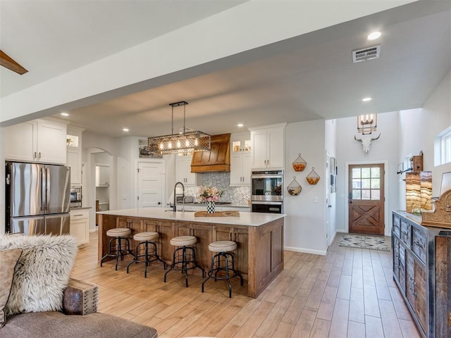 kitchen featuring a chandelier, light wood-style flooring, a kitchen bar, backsplash, and appliances with stainless steel finishes