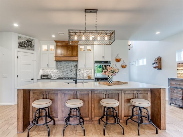 kitchen with a large island with sink, stainless steel double oven, visible vents, and light wood-type flooring