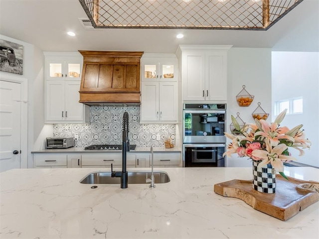 kitchen featuring stainless steel double oven, backsplash, visible vents, a sink, and custom exhaust hood