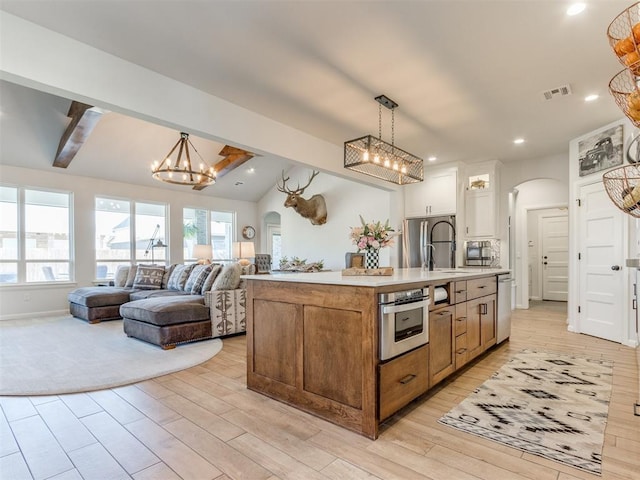 kitchen featuring arched walkways, an inviting chandelier, light wood finished floors, light countertops, and appliances with stainless steel finishes