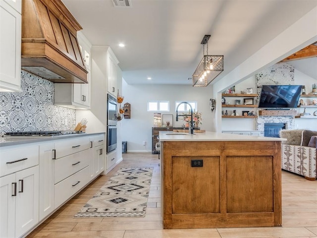 kitchen featuring light wood-style flooring, a sink, a kitchen island, appliances with stainless steel finishes, and premium range hood