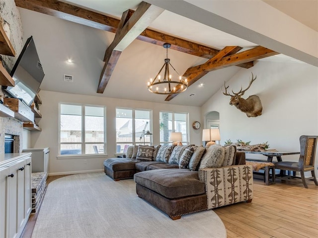 living area with a stone fireplace, an inviting chandelier, light wood finished floors, beamed ceiling, and visible vents
