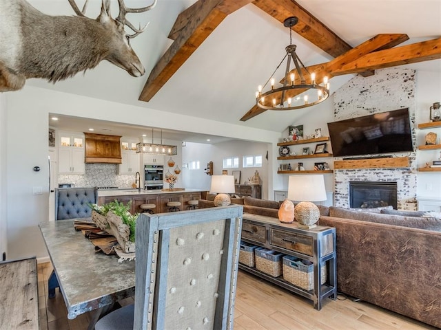 living room featuring light wood finished floors, a tiled fireplace, an inviting chandelier, beamed ceiling, and high vaulted ceiling